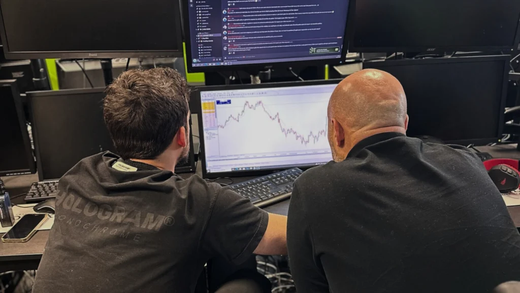 Deux traders en formation analysent un graphique boursier en temps réel sur plusieurs écrans dans une salle de marché.